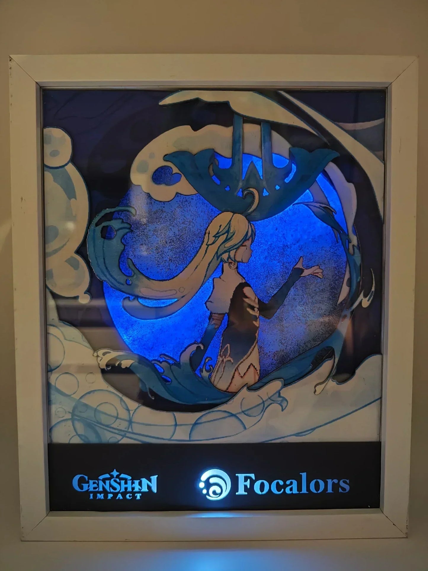 Lightbox accesa dedicata a Focalors da Genshin Impact, con effetto LED blu brillante che illumina l'Arconte di Fontaine circondata da elementi acquatici e simboli stilizzati.