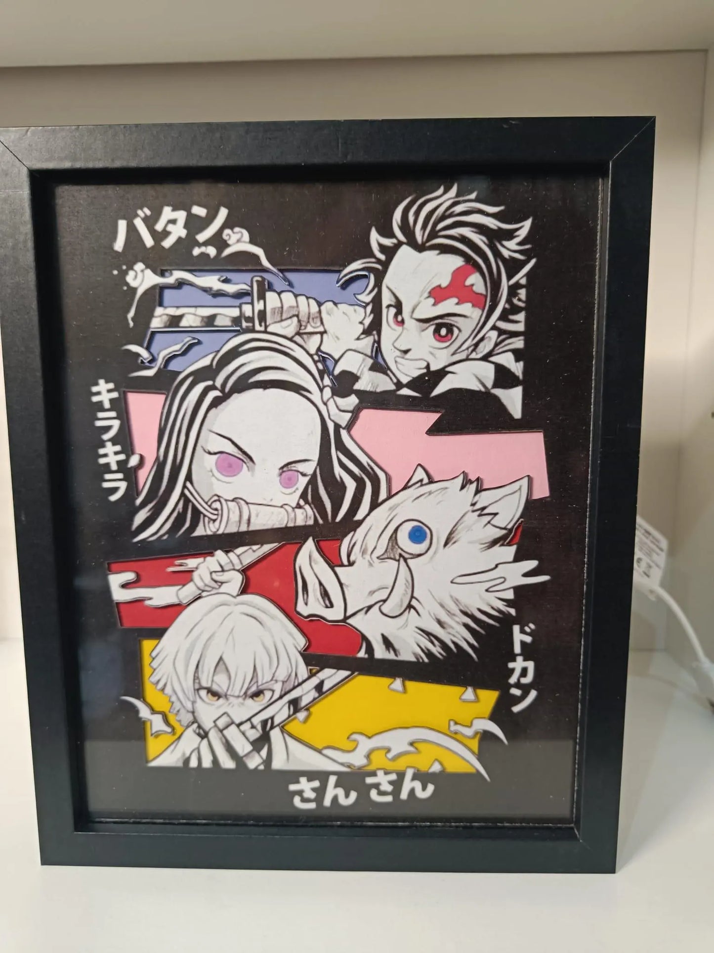 Cornice luminosa artigianale ispirata a Demon Slayer con Tanjiro, Nezuko, Inosuke e Zenitsu. Luci LED calde e dettagli a più livelli.