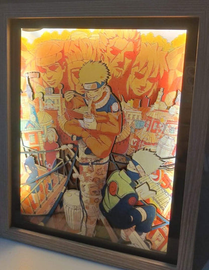Questa opera d'arte illuminata e incorniciata intitolata "Naruto - Naruto Uzumaki" di L'Atelier di Zelda raffigura Naruto in un abito arancione che mangia noodles sullo sfondo del Villaggio della Foglia. Un personaggio in verde recita sotto, con colori caldi ed elementi stratificati che creano un effetto 3D.