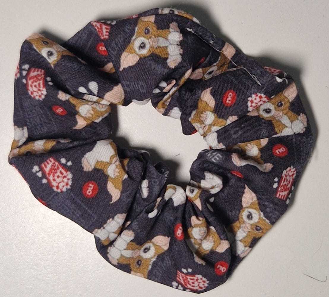 Lo scrunchie Gremlins Gizmo di L'Atelier di Zelda presenta un design fatto a mano con uno sfondo scuro che mette in risalto i motivi Gizmo e popcorn, aggiungendo un tocco giocoso a qualsiasi outfit.