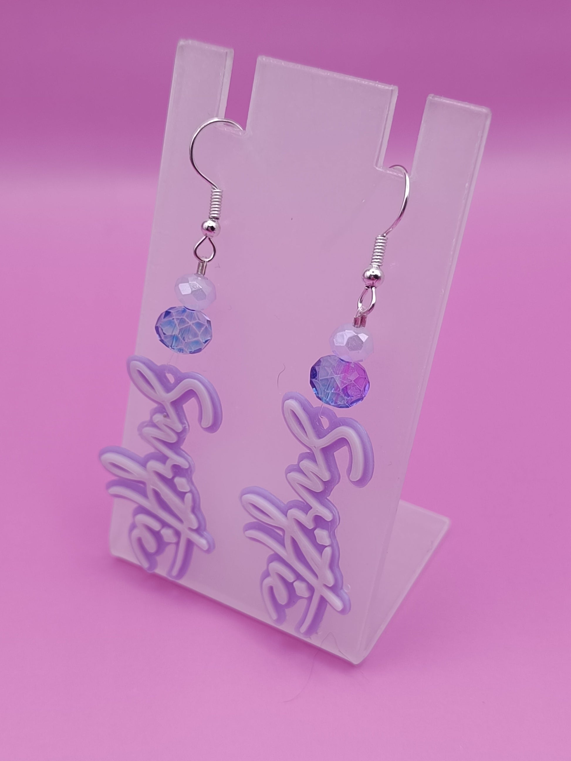 Orecchini artigianali "Swiftie" ispirati a Taylor Swift su sfondo rosa con design lilla, per fan del pop.