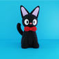 Statua artigianale di Jiji in PLA stile crochet con fiocco rosso, su licenza NaraaPrints, su sfondo azzurro